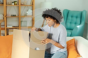 African girl unpacking delivery looking in box. Happy woman opening carton box. Female getting parcel looking at