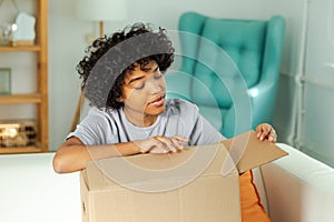 African girl unpacking delivery looking in box. Happy woman opening carton box. Female getting parcel looking at