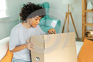 African girl unpacking delivery looking in box. Happy woman opening carton box. Female getting parcel looking at