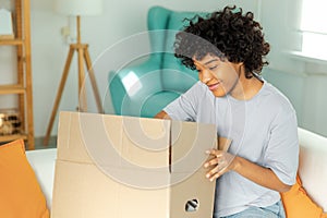 African girl unpacking delivery looking in box. Happy woman opening carton box. Female getting parcel looking at