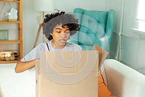 African girl unpacking delivery looking in box. Happy woman opening carton box. Female getting parcel looking at