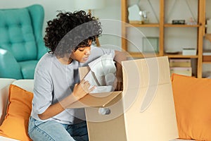 African girl unpacking delivery looking in box. Happy woman opening carton box. Female getting parcel looking at