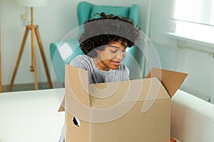 African girl unpacking delivery looking in box. Happy woman opening carton box. Female getting parcel looking at