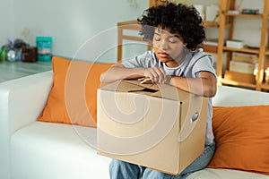 African girl unpacking delivery looking in box. Happy woman opening carton box. Female getting parcel looking at