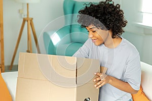 African girl unpacking delivery looking in box. Happy woman opening carton box. Female getting parcel looking at