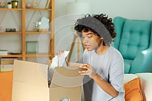 African girl unpacking delivery looking in box. Happy woman opening carton box. Female getting parcel looking at