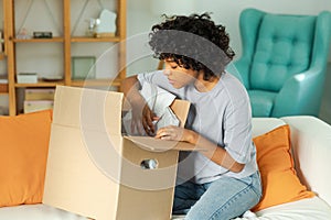 African girl unpacking delivery looking in box. Happy woman opening carton box. Female getting parcel looking at