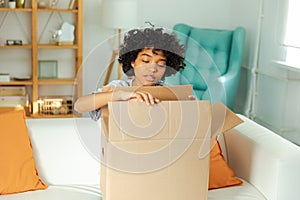 African girl unpacking delivery looking in box. Happy woman opening carton box. Female getting parcel looking at