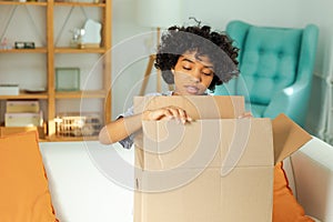 African girl unpacking delivery looking in box. Happy woman opening carton box. Female getting parcel looking at