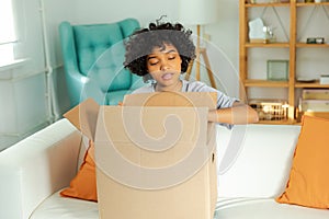African girl unpacking delivery looking in box. Happy woman opening carton box. Female getting parcel looking at