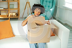 African girl unpacking delivery looking in box. Happy woman opening carton box. Female getting parcel looking at