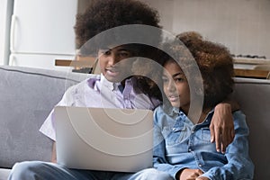 Young African couple sit on sofa using laptop