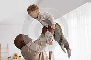 African Grandpa Holding Little Grandson Up In Air At Home