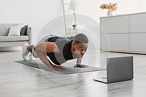 African Guy Doing Push-Ups Exercise Near Laptop On Floor Indoor