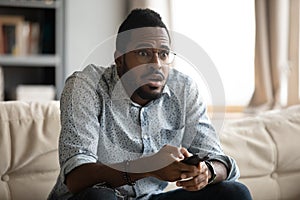 African guy holding remote control watching movie feels appalled