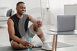African Guy Holding Smartphone Watching Online Training On Laptop Indoors