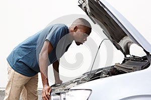 African guy looking under the hood of his broken down car