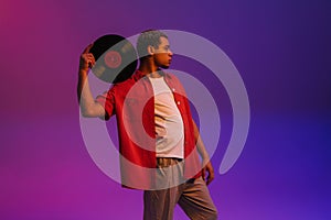 African guy posing with vinyl record isolated over purple neon background