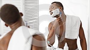 African Guy Shaving Face Covered With Shave Foam In Bathroom