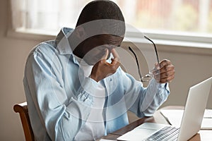 African guy sit near laptop taking off glasses reduce eyestrain