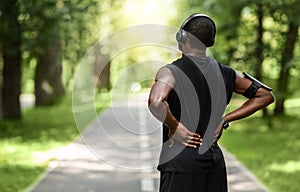 African guy sportsman rubbing his back, exercising at park