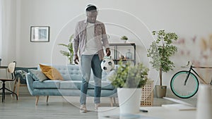 African guy wearing wireless headphones having fun kicking ball in apartment