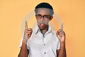 African handsome man pointing up with fingers in shock face, looking skeptical and sarcastic, surprised with open mouth