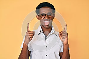 African handsome man pointing up with fingers sticking tongue out happy with funny expression