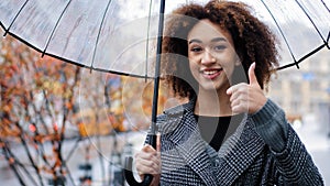 African happy successful girl curly multiracial woman holding transparent umbrella posing in autumn city in rain looking