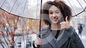 African happy successful girl curly multiracial woman holding transparent umbrella posing in autumn city in rain looking