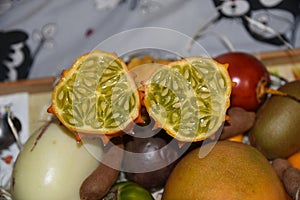 African horned cucumber, exotic fruit cut in two halves on the plate with other fruits on the light background