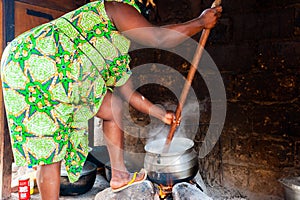 African housewife in traditional clothes cooking foufouwith wooden mortar in home kitchen in cameroon