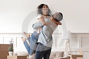 African husband lifting happy wife celebrating moving day with boxes