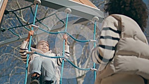 African kid climbing rope ladder sunny day. Little girl playing on playground