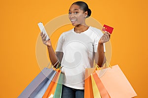 African lady with bags in hands showcasing credit card, studio