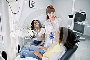 African lady mother and child girl at appointment in modern pediatric dentistry clinic. Female doctor makes dental