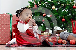 African little girl child eating apple and sitting on floor at living room with many present gift boxes under beautiful decorative