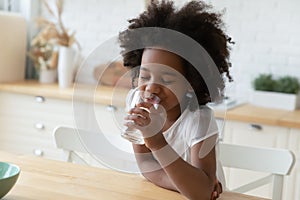 African little girl drinking natural water seated in kitchen