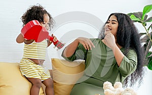 African little girl and mother playing ukulele together and smiling with happiness while doing leisure in living room at home on