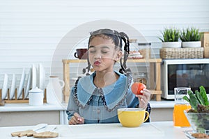 African little kid girl having fun with food and vegetables at kitchen, holding tomato, make a pucker lips, kissing. Cute child