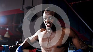 African man is boxer proficient in boxing, Breathing heavily after boxing match in boxing ring in hot gym, man leaning on edge photo
