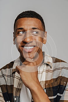 African man in checkered shirt looking aside smiling with hand on chin while standing isolated