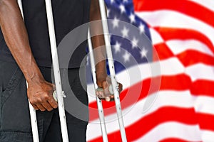 African man with crutch on the background of the USA flag. Disabled veterans of the US Army. The concept of violence and racism in
