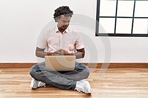 African man with curly hair using laptop sitting on the floor with hand on stomach because nausea, painful disease feeling unwell