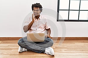 African man with curly hair using laptop sitting on the floor touching mouth with hand with painful expression because of