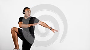 African Man Doing Elbow To Knee Exercise Wearing Headphones, Studio