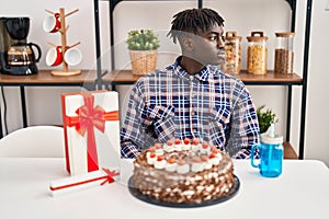 African man with dreadlocks celebrating birthday holding big chocolate cake looking to side, relax profile pose with natural face