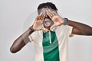 African man with dreadlocks standing over isolated background shouting angry out loud with hands over mouth