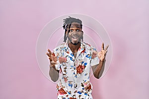 African man with dreadlocks wearing summer shirt over pink background celebrating victory with happy smile and winner expression
