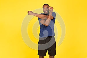 African Man Exercising Stretching Arms Having Fitness Workout, Yellow Background